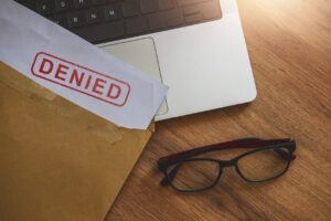 An open folder on a desk that says "Denied", next to a laptop and pair of glasses