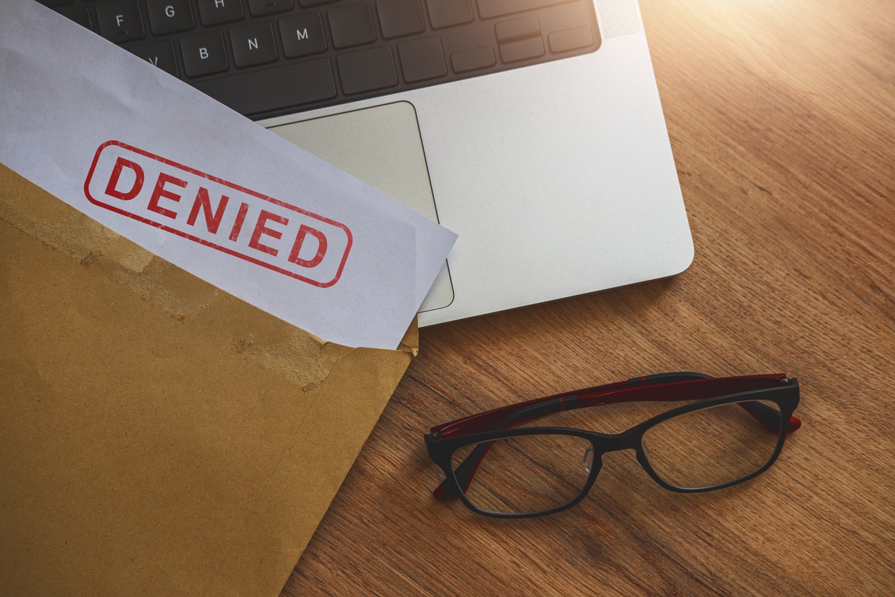 An open folder on a desk that says "Denied", next to a laptop and pair of glasses
