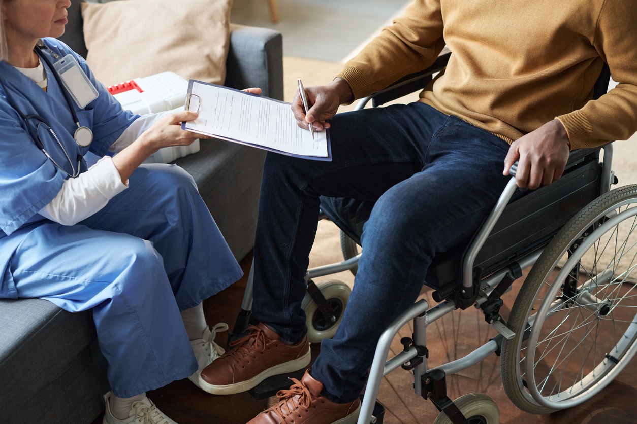 Person in a wheelchair signing a document being held by someone else