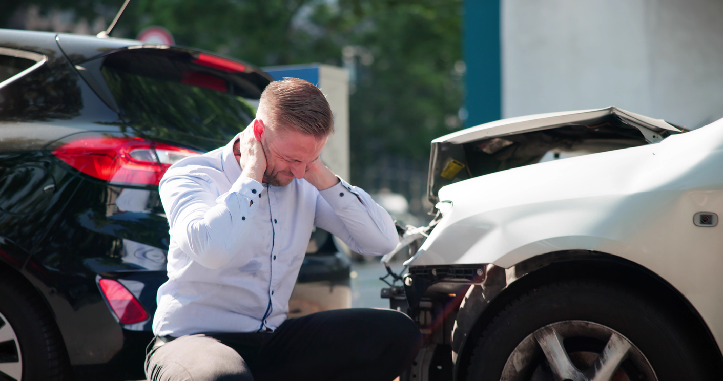 Man holding the back of his neck next to a car crash